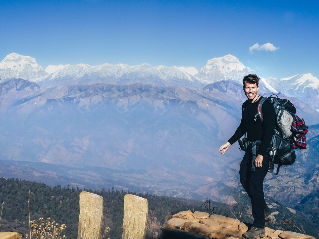 Travel backpack and trekking boots recommendation. A man stands on the peak of a mountain doing the ABC trek in Nepal