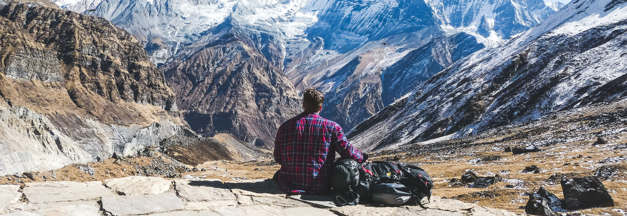 Travel backpack and trekking boots recommendation. A person sits at the peak of the ABC trek in Nepal looking over the mountains
