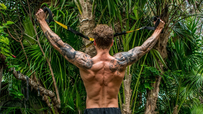 How to use a TRX: Why you're performing TRX wrong. Man performs a TRX Y movement in a jungle