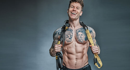 Coach Adam aka TRX Traveller holds a TRX suspension Trainer over his shoulders and smiles